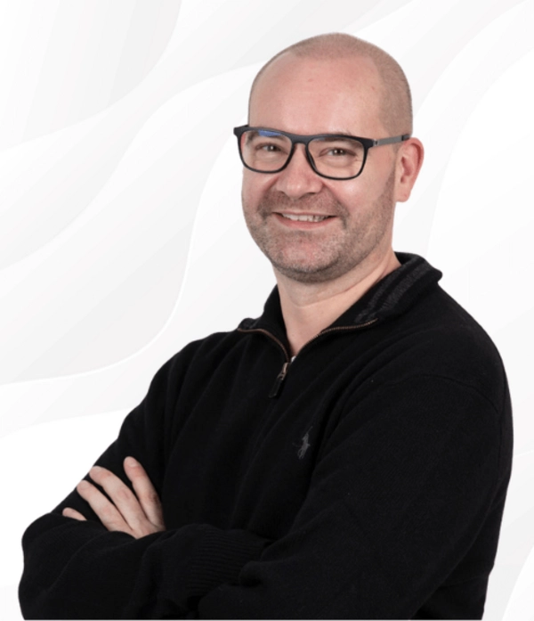 Christian Heutger, Trainer bei PSW TRAINING, lächelt mit verschränkten Armen in schwarzer Kleidung vor hellem Hintergrund.