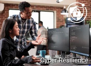 Zwei Personen analysieren Code an Monitoren als Darstellung von Cyber Resilience, ergänzt durch Schloss-Symbol für IT-Sicherheit und Schutz digitaler Systeme.