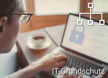 Person arbeitet an einem Laptop mit sichtbarem Schloss-Symbol auf dem Bildschirm, oben eingeblendetes Netzwerksymbol – Darstellung für Schulung im Bereich IT-Grundschutz.