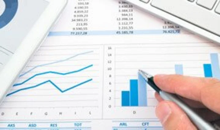 Hand mit Stift über Tabellen- und Balkendiagrammen, daneben technische Geräte – Darstellung für Revisionsfähigkeit und nachvollziehbare Dokumentation von Daten und Prozessen.