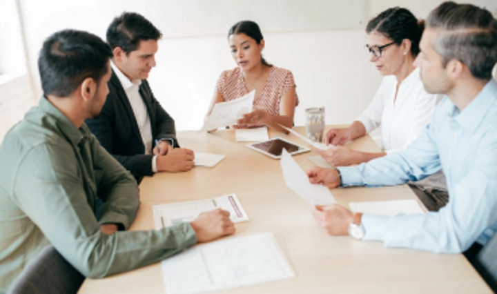 Auditteam in Besprechung prüft gemeinsam Dokumente am Tisch als Symbol für ein internes oder externes Audit nach ISO 27001 oder ISO 42001.