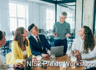 Personengruppe in Besprechungssituation mit Laptop und Getränken, eine Person präsentiert stehend, eingeblendeter Text „NIS2-Praxis Workshop“ – Darstellung eines interaktiven Workshops zur praktischen Umsetzung der NIS2-Richtlinie.